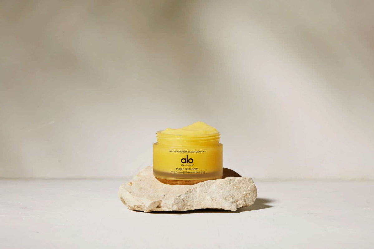 Shot of opened Magic Multi-Balm resting on a beige rock. 