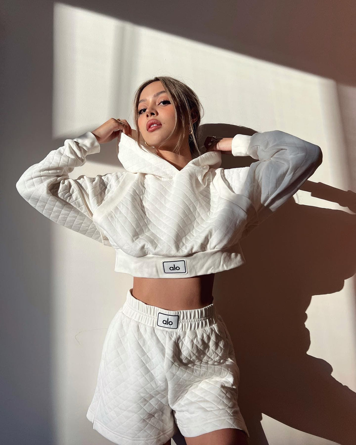 @lilymaymac wearing the Quilted Arena Boxing Short and matching Quilted Cropped Arena Hoodie in Ivory while posing against a white wall.  